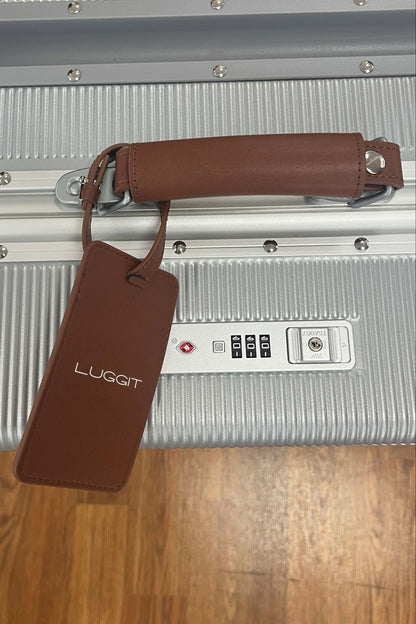 Silver suitcase with a brown handle and luggage tag on a wooden floor.