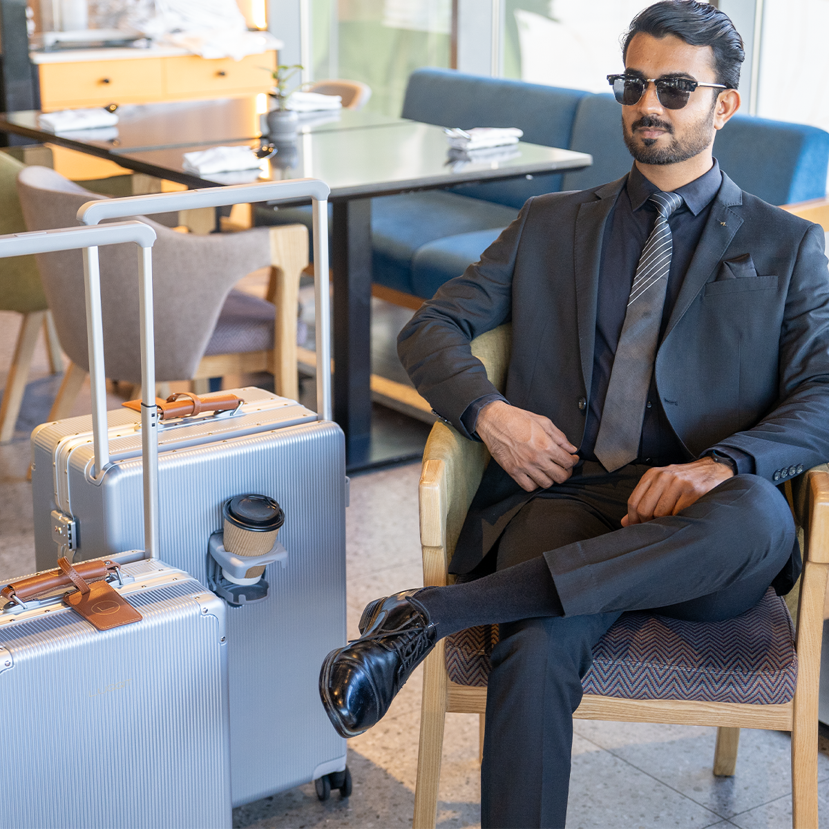 A person in a suit sitting in a chair with LUGGIT branded silver luggage pieces beside them.