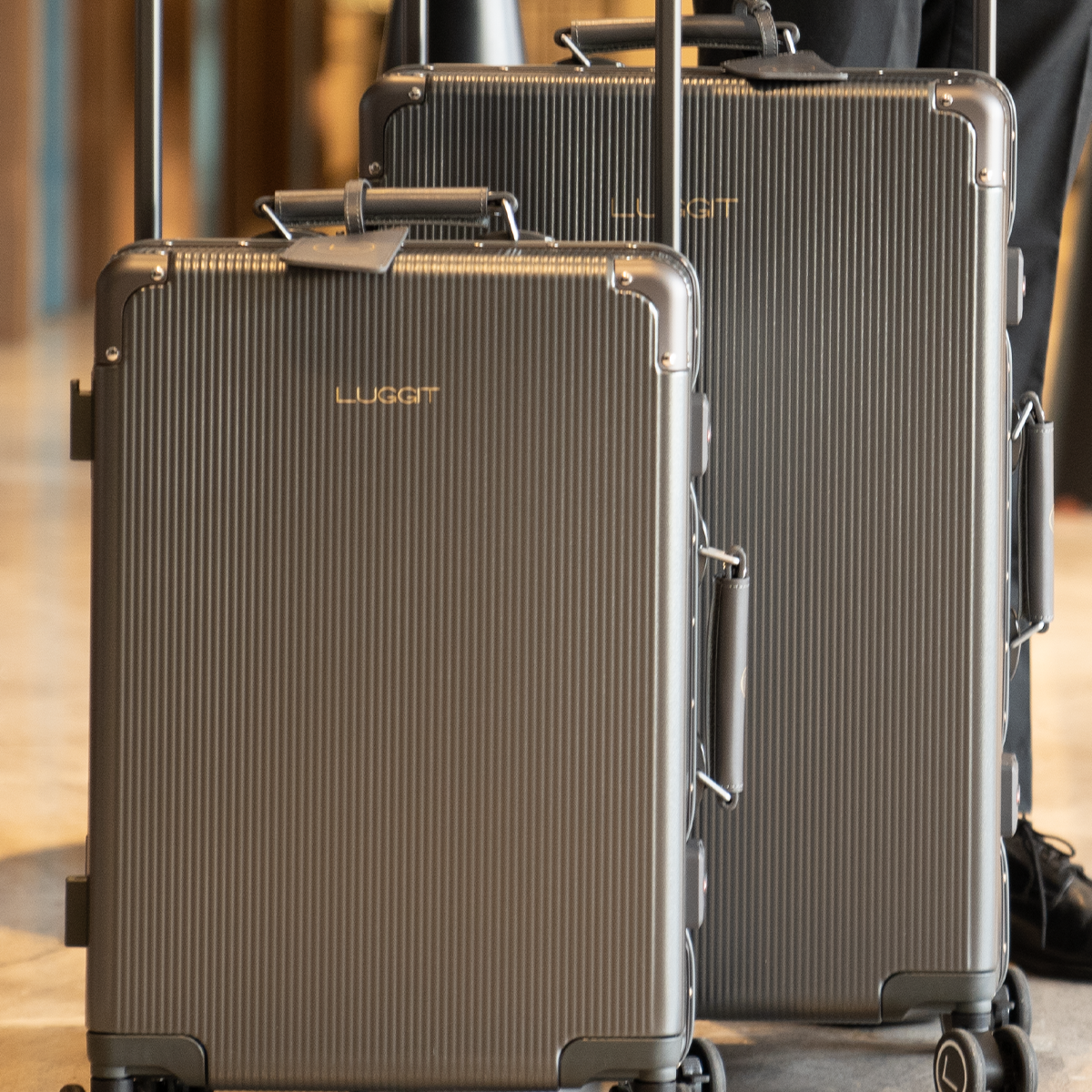 Two gray LUGGIT luxury suitcases with a hard-shell construction, wide telescopic handles, and rolling wheels.